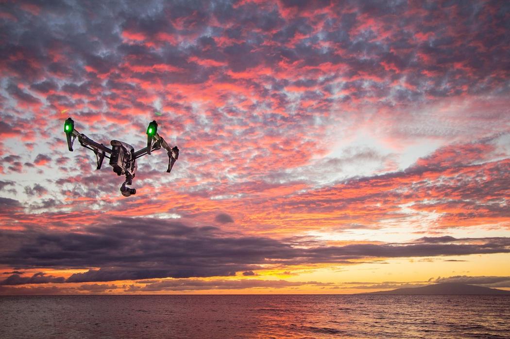 un drone volant au dessus de l'eau pendant un coucher de soleil